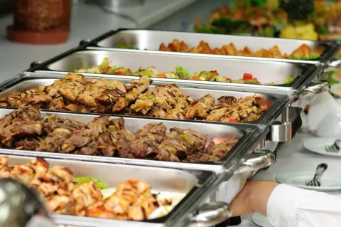 A person is taking a tray of food from a buffet line.