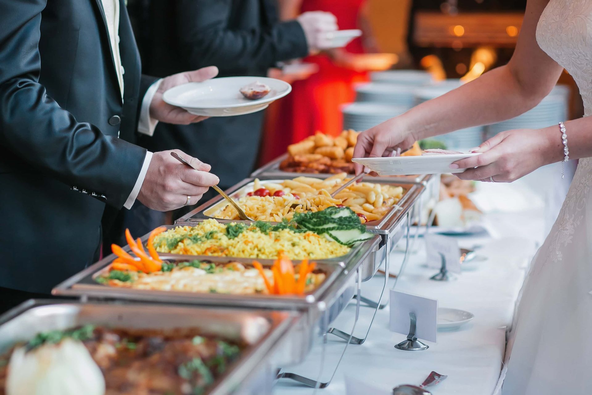 A bride and groom are taking food from a buffet at a wedding reception.