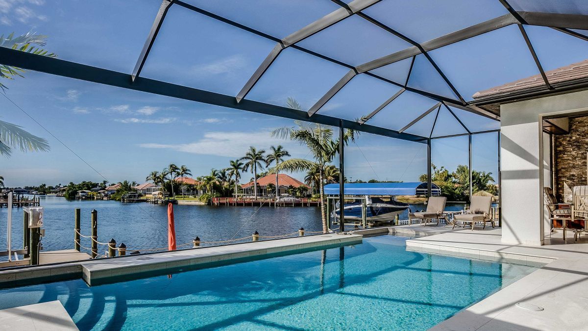 A large swimming pool is surrounded by a screened in area with a view of the water.