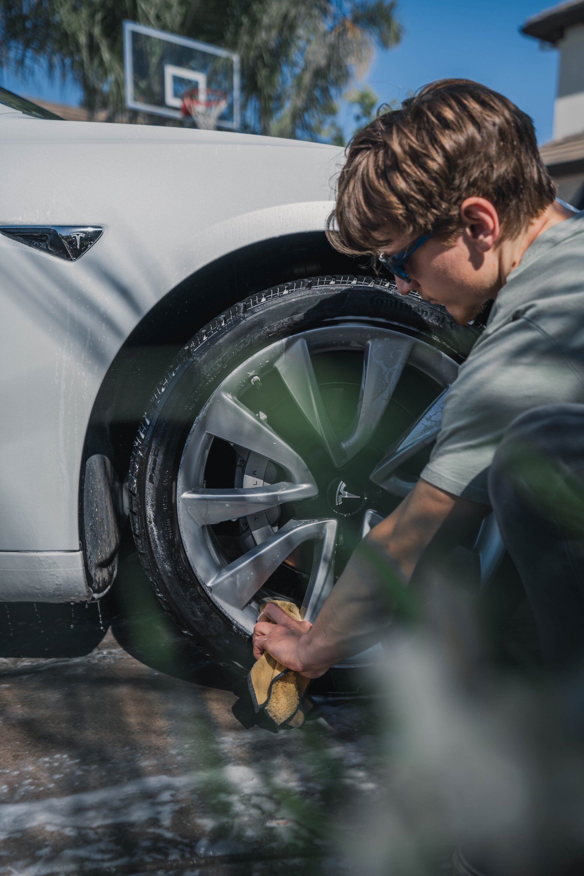Person washing the tire of a white car outside, using a sponge.