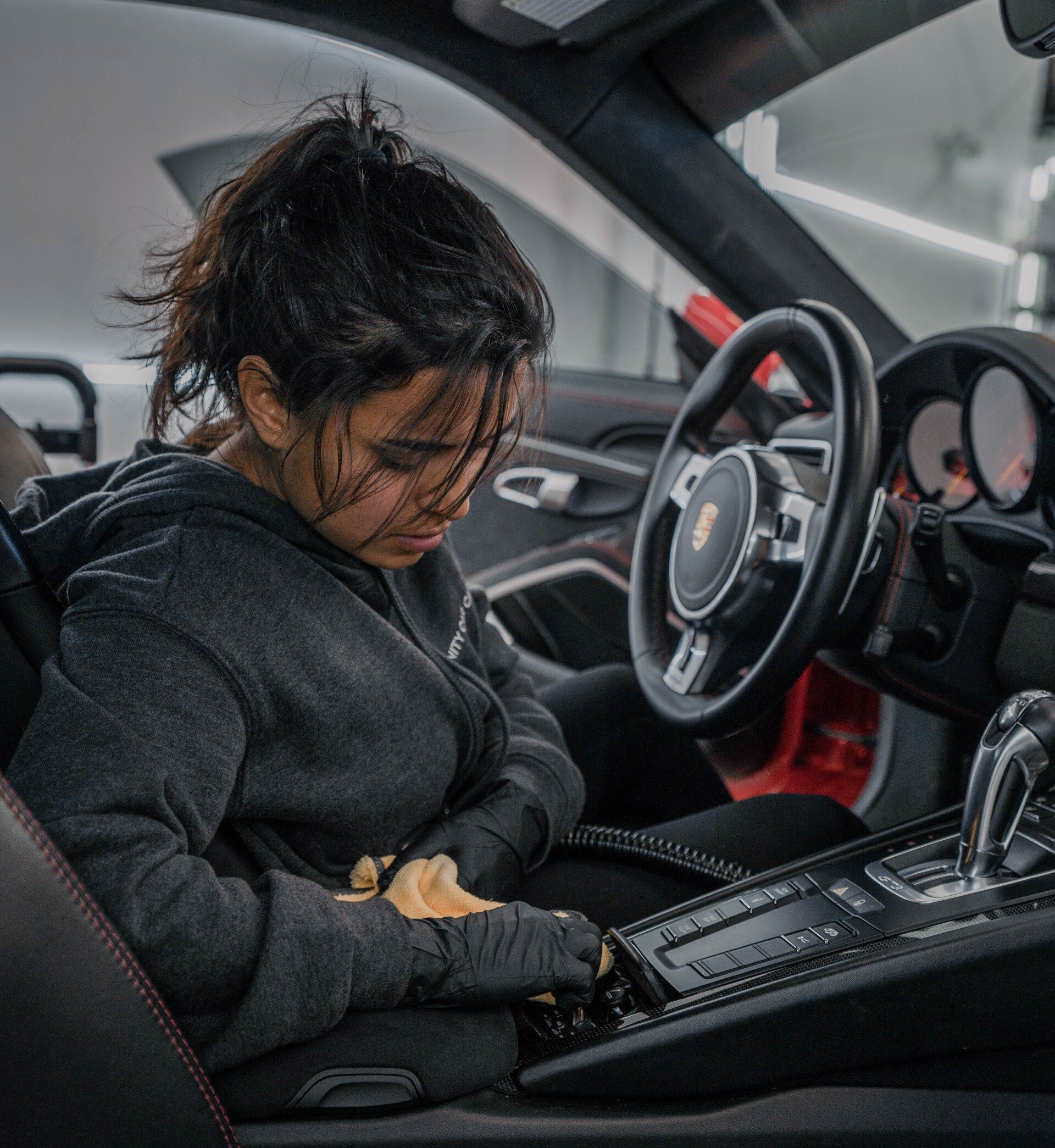 Person working on the interior of a Porsche car. They wear a gray hoodie, inside the car cabin.