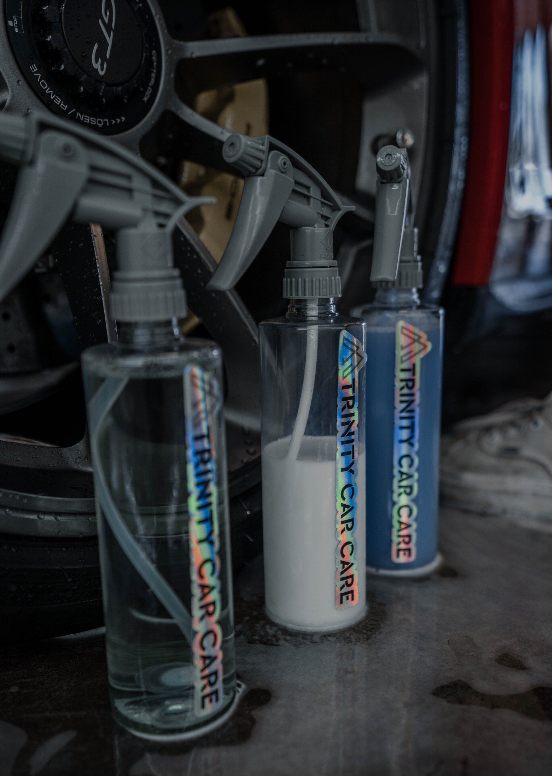 Three Trinity Car Care spray bottles lined up next to a car tire.