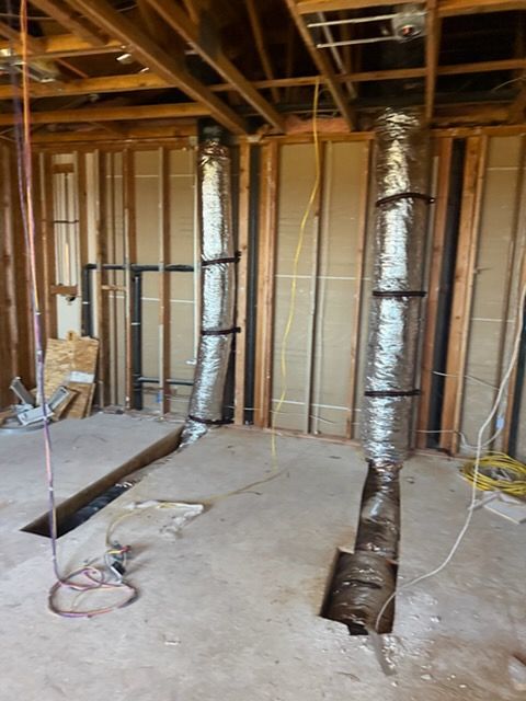 A construction site showing two vertical HVAC ducts running from the floor into the open ceiling joists.