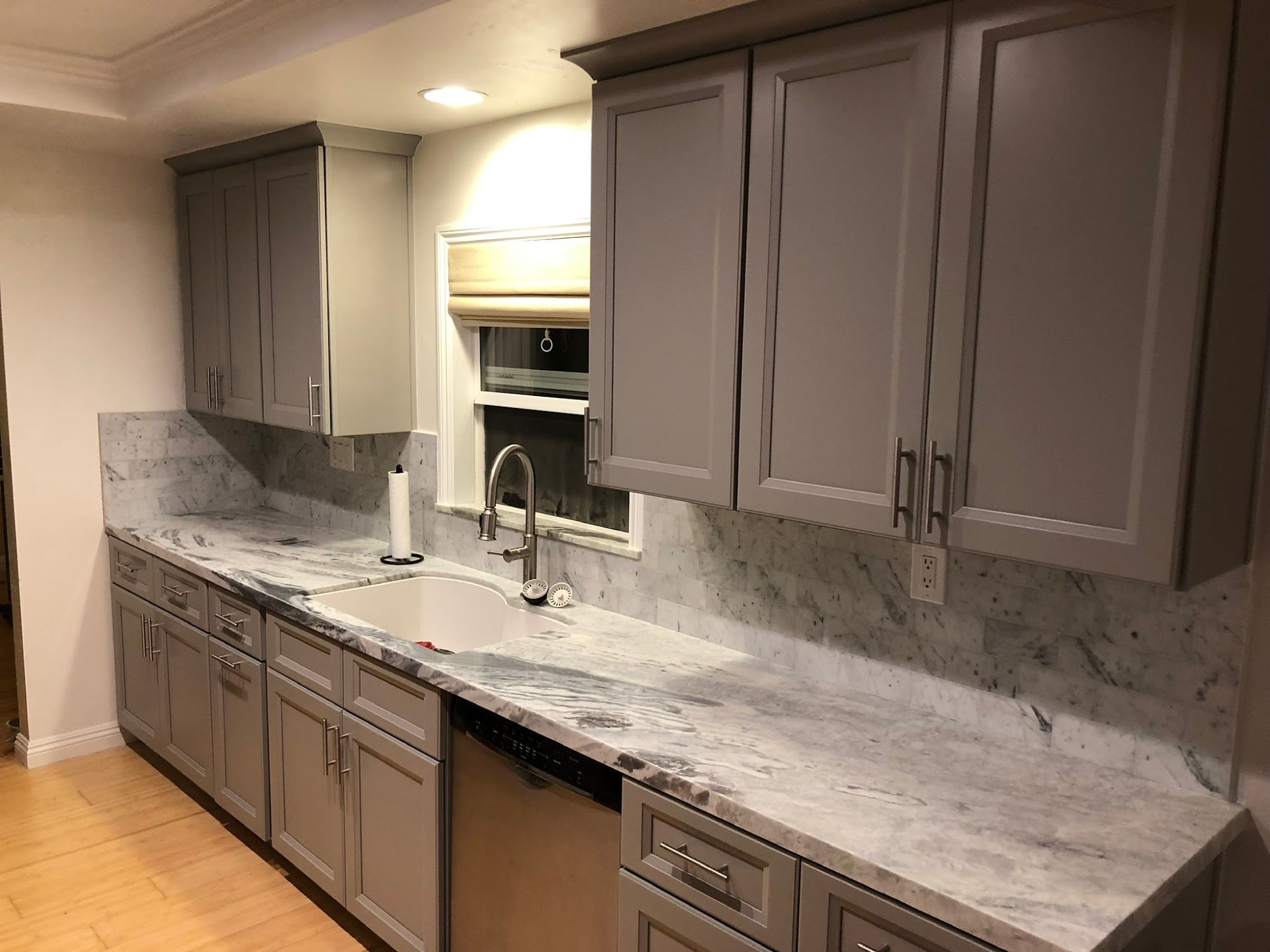 A kitchen with gray cabinets , white counter tops , a sink and a dishwasher.