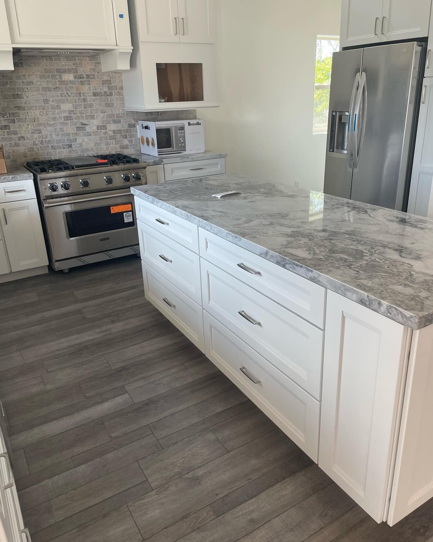 A kitchen with white cabinets , granite counter tops , stainless steel appliances and a large island.