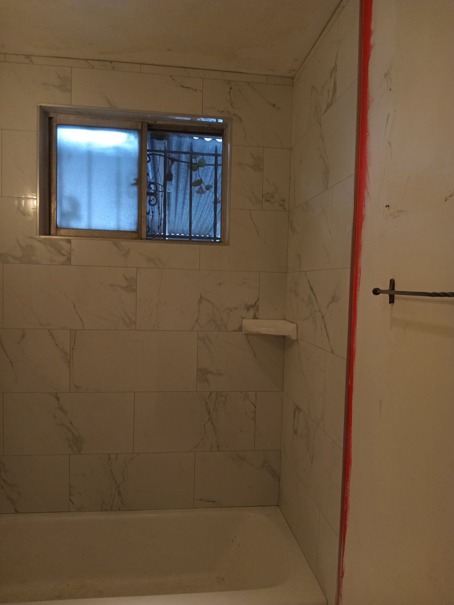 Bathroom with white marble-look tile, window with metal bars, towel bar, and a partially open door.