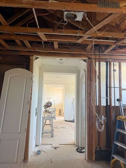 Construction site showing a doorway leading into a room with a work table, exposed ceiling joists, and loose wiring.