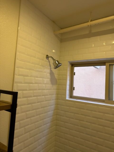 A shower head mounted on a white, subway-tiled wall next to a window in a bathroom.