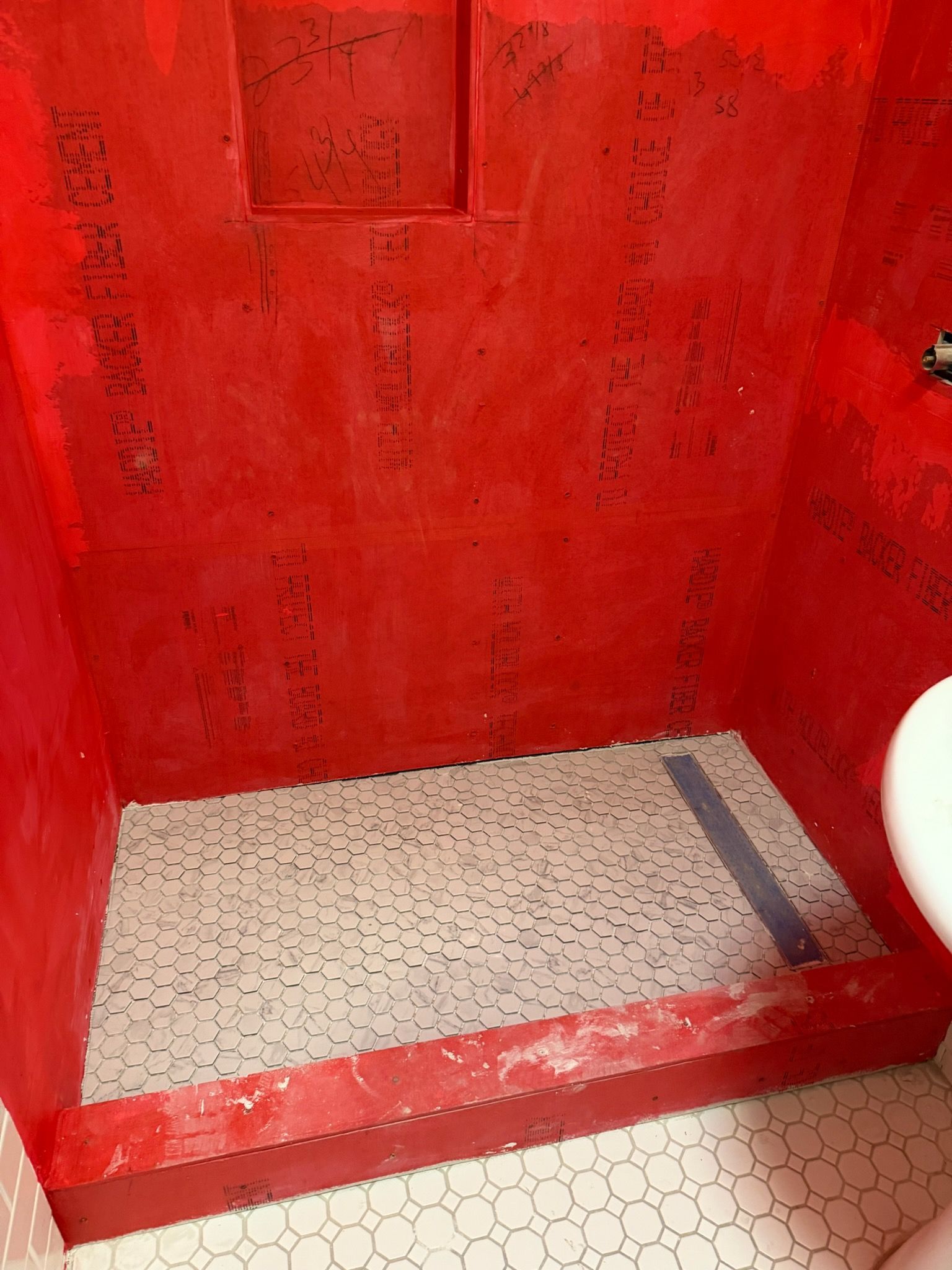 A shower stall under construction with red waterproofed walls, a tiled floor, and a linear drain.