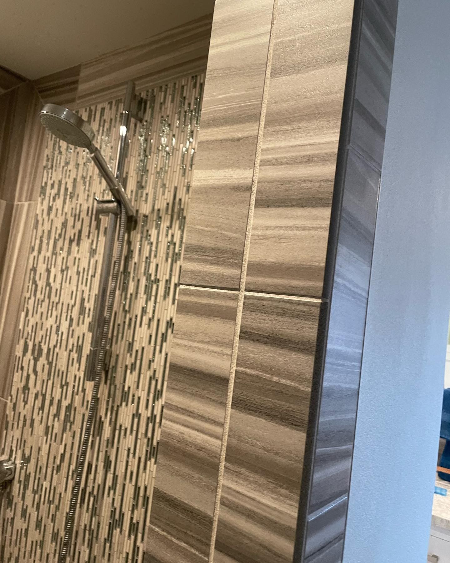 A shower with a striped tile wall and a shower head