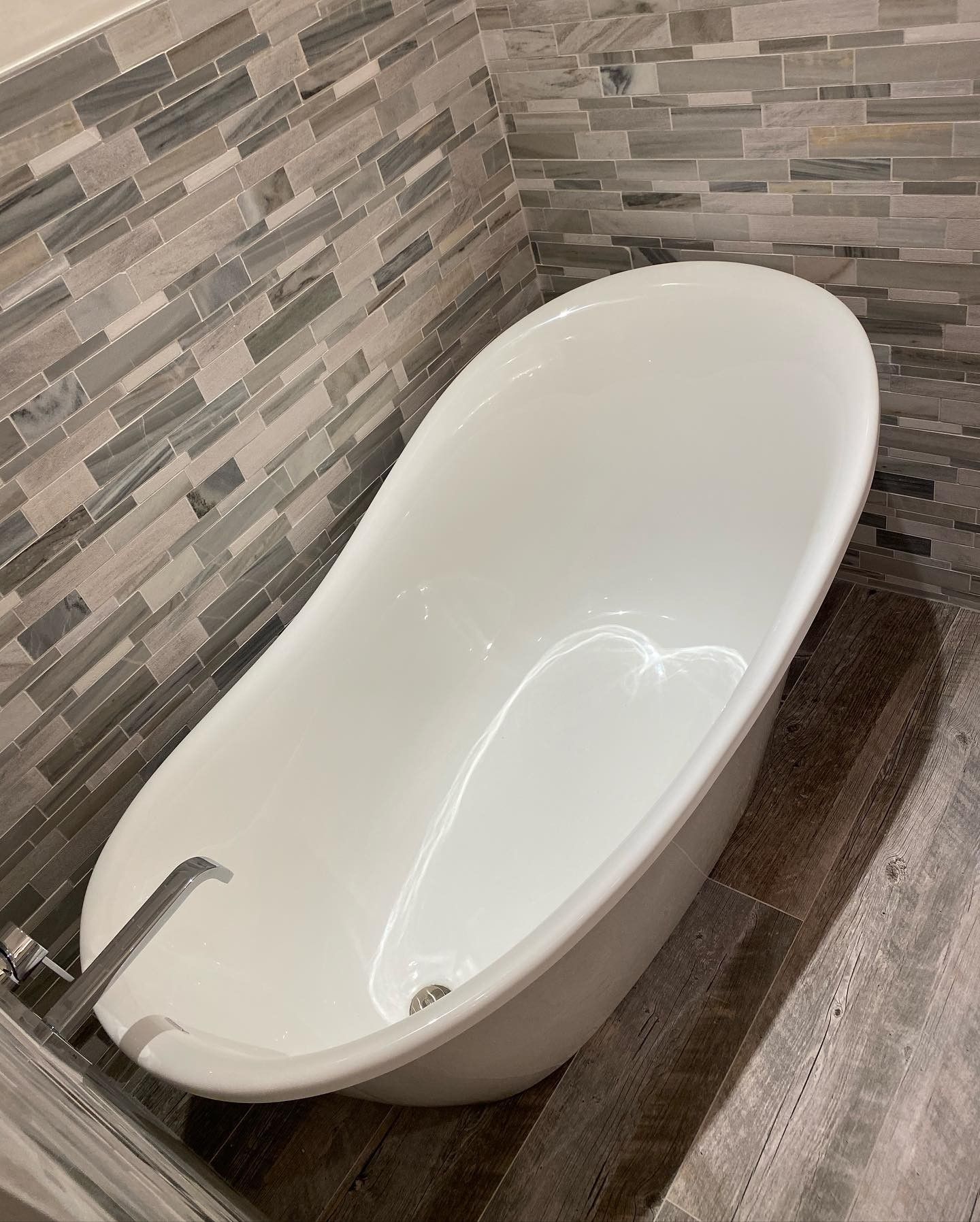 A white bathtub is sitting in a bathroom next to a stone wall.