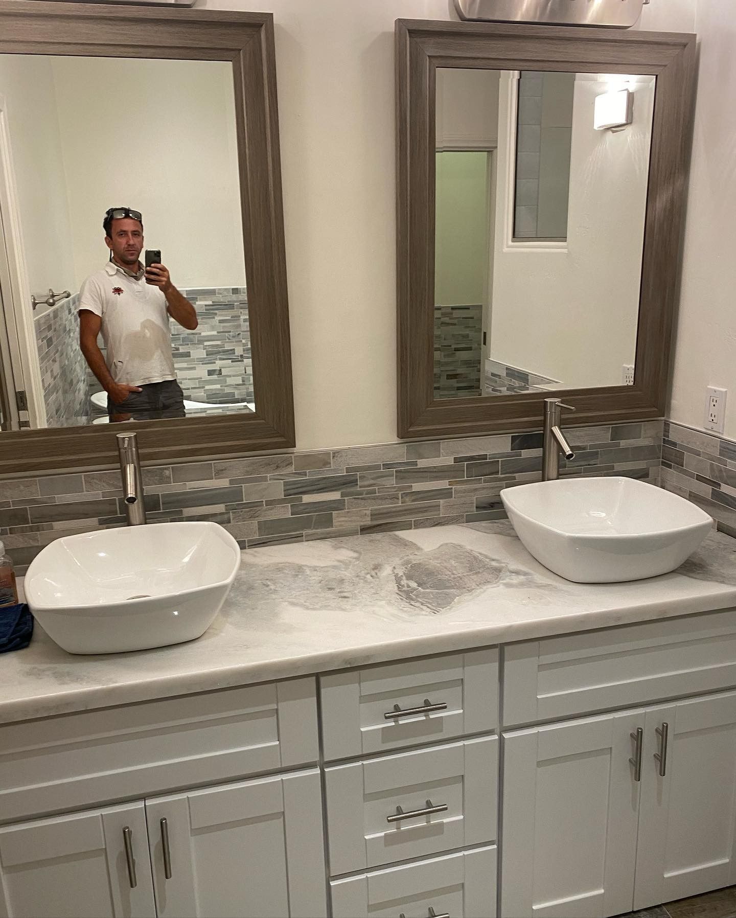 A man is taking a picture of himself in a bathroom with two sinks and two mirrors.