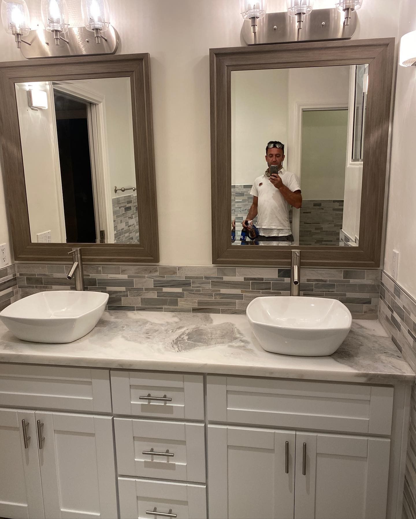 A man is taking a picture of himself in a bathroom with two sinks and two mirrors.