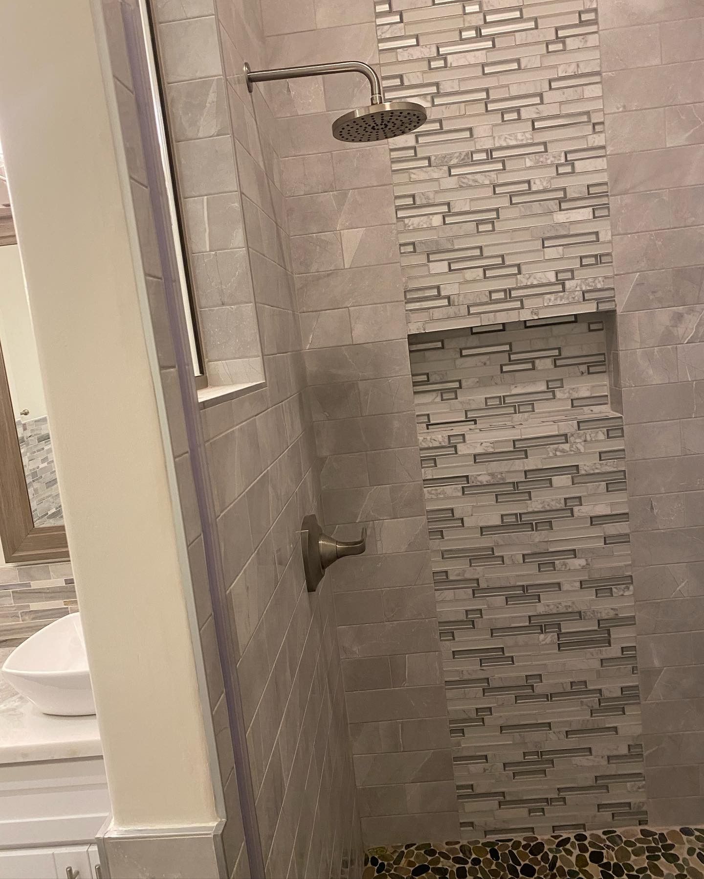 A bathroom with a shower , sink , mirror and shower head.