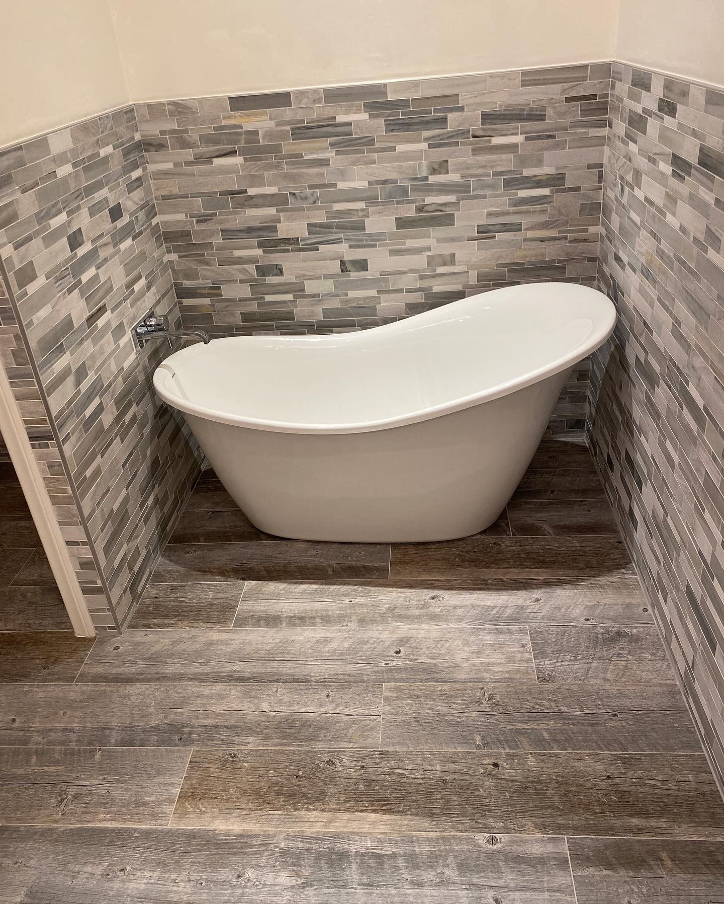 A bathtub is sitting in a corner of a bathroom next to a stone wall.