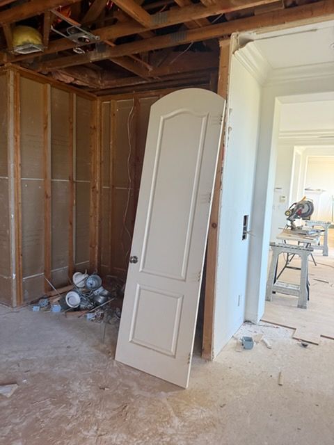 An off-white arched door leans against a partially framed interior wall in a room undergoing renovation.