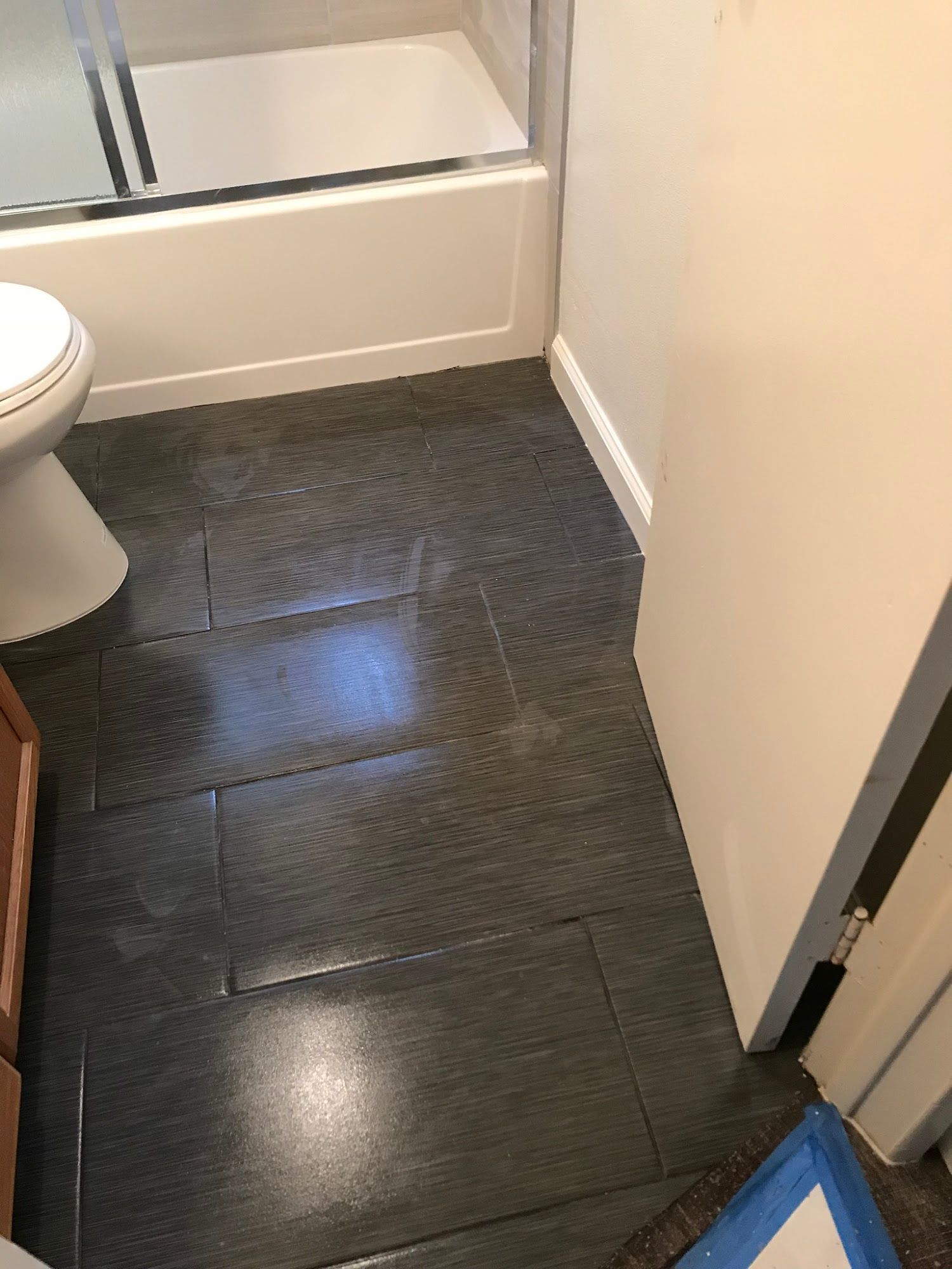 A bathroom with a toilet , bathtub , and black tile floor.