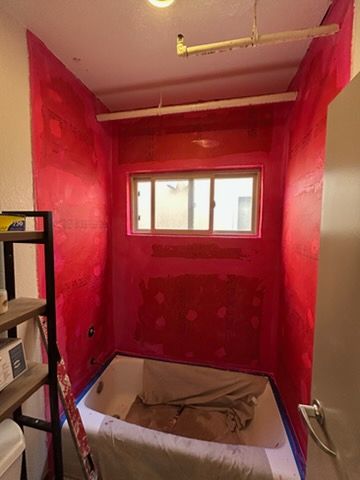 A bathroom alcove with a white bathtub covered in a drop cloth, surrounded by walls painted in bright red waterproof sealant.
