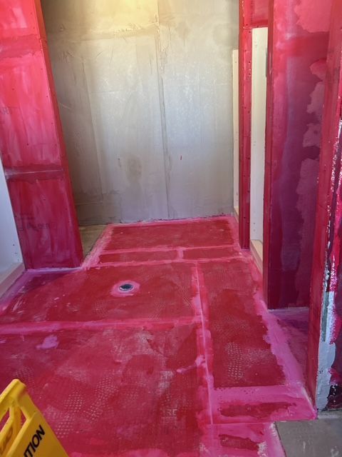 Red waterproof membrane applied to the floor and walls of a shower. Construction site.