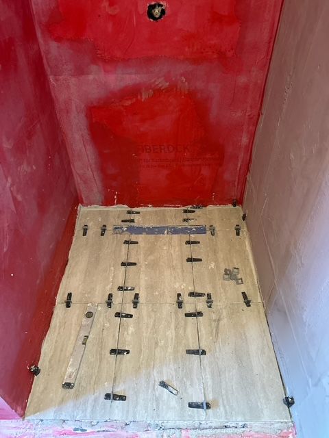 Inside view of a shower stall with plywood on the floor, red walls, and black spacers.