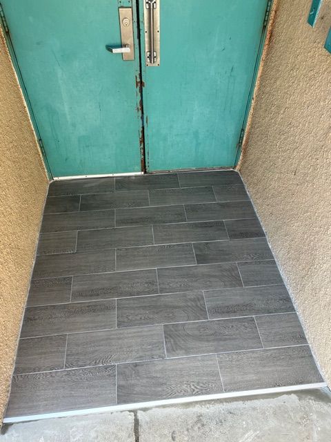 Gray tiled entrance to teal double doors with metal threshold.