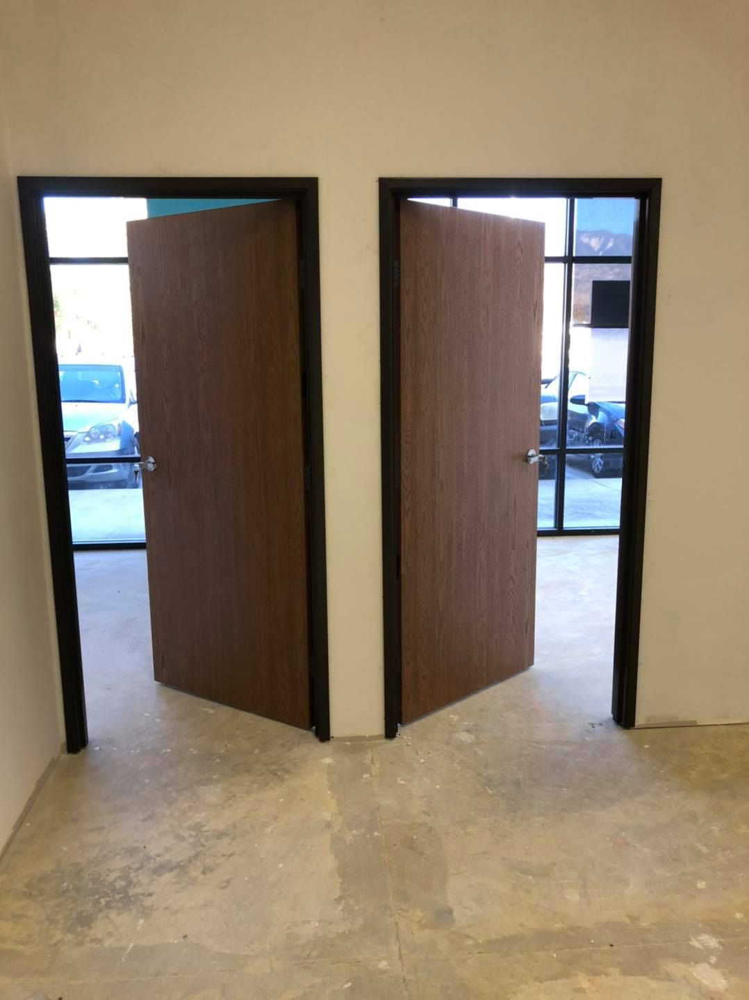 Two doors are open in a room with a car parked in the background.