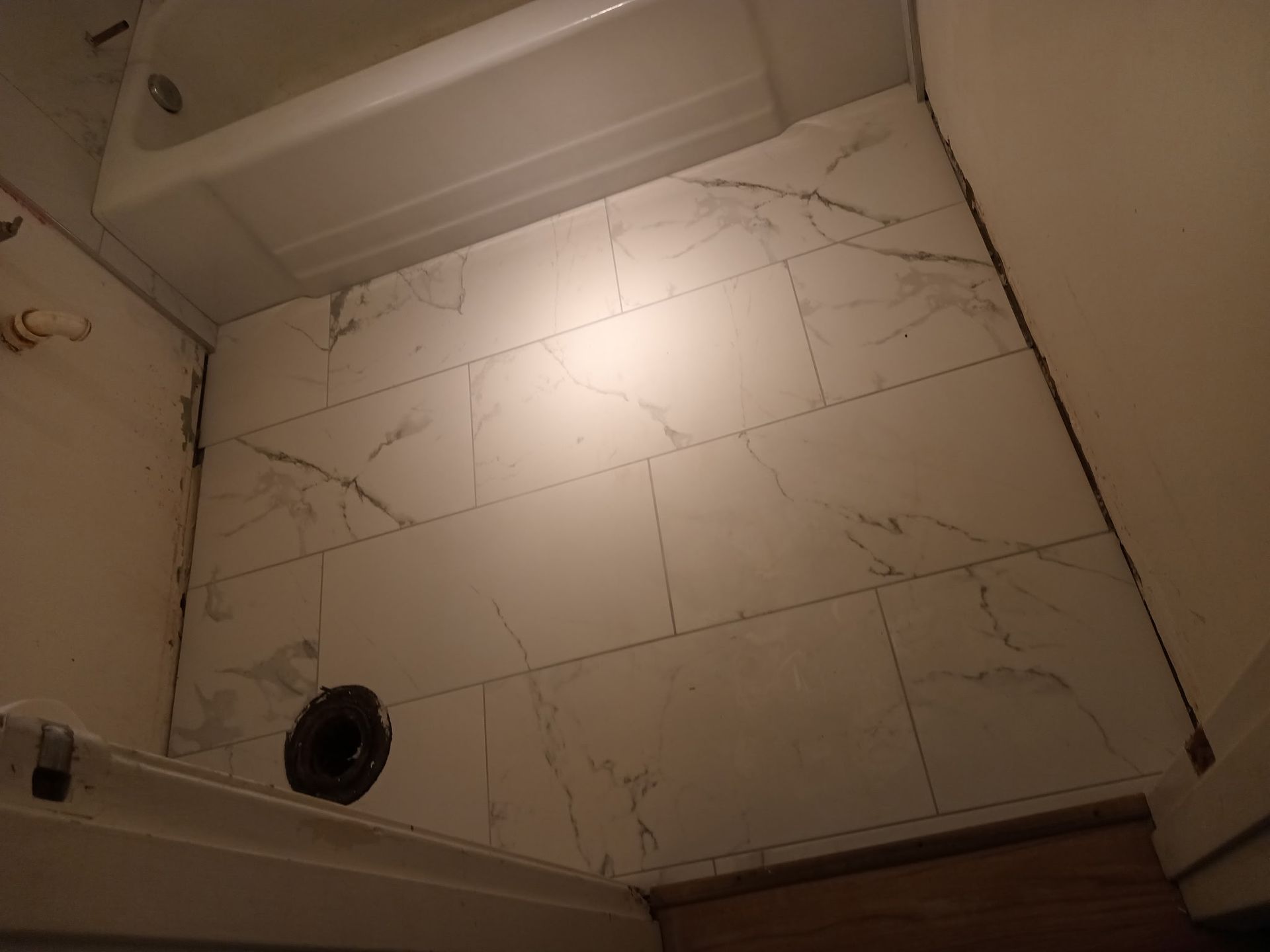 Bathroom floor with white marble-like tiles and a black drain, adjacent to a white bathtub.