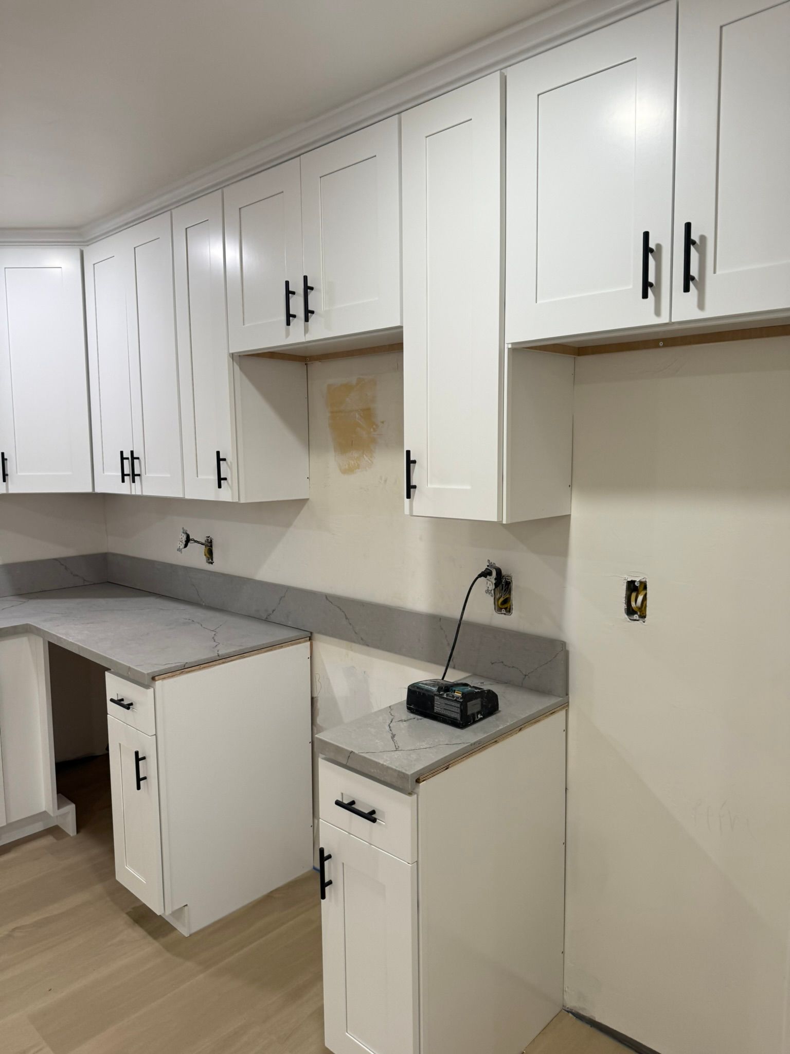 White kitchen cabinets with black handles and grey countertops in a kitchen under construction.