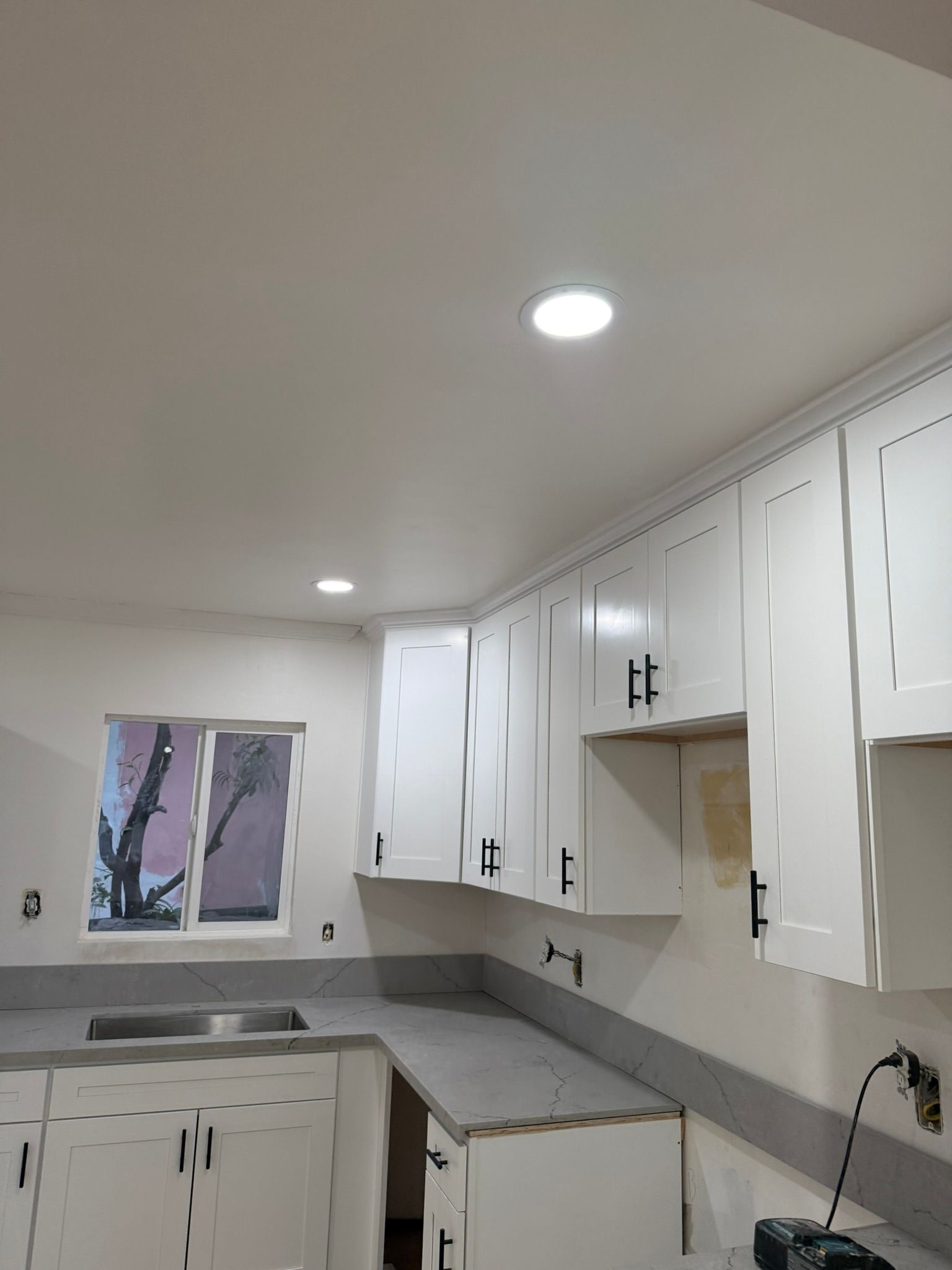 A kitchen with white cabinets, grey countertops, a sink, and recessed ceiling lighting.