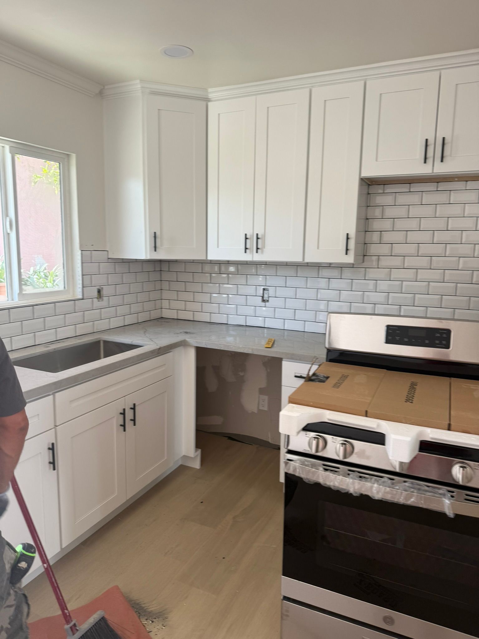 A renovated kitchen featuring white cabinets, gray countertops, a subway tile backsplash, and a new stainless steel stove.