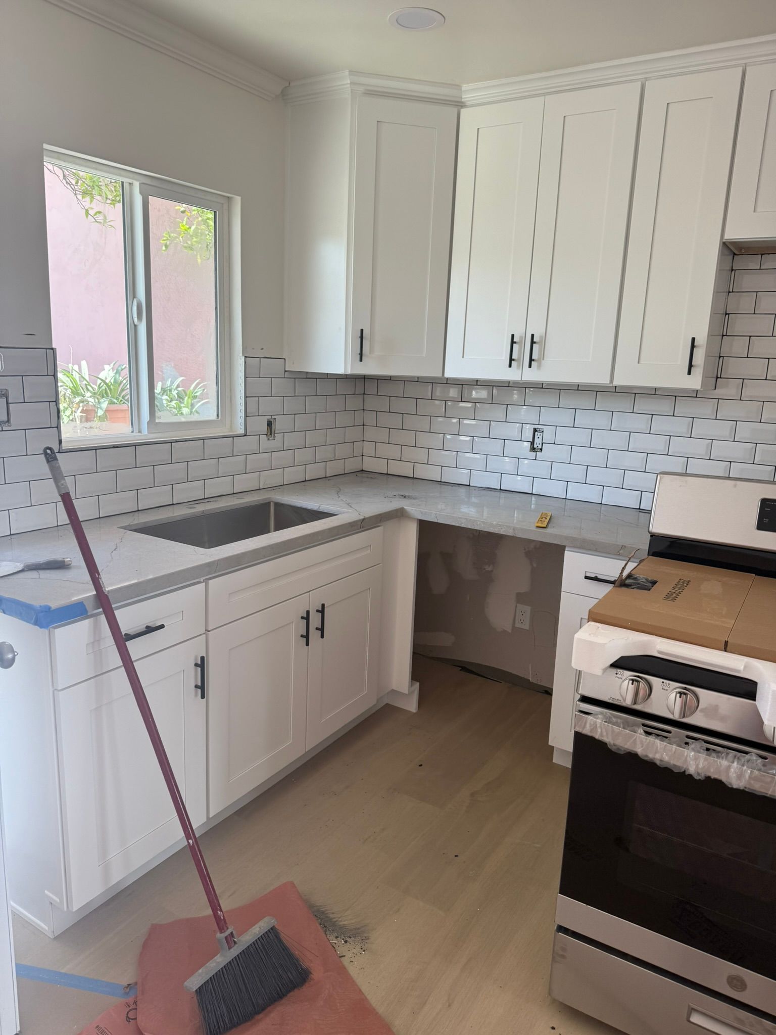 A renovated kitchen with white cabinets, light countertops, newly installed subway tile backsplash, and a stainless stove.