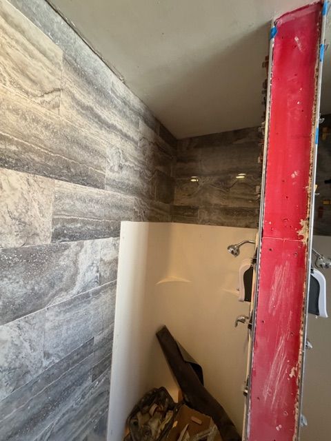 Bathroom shower area with tiled wall, white shower basin, and red construction element.