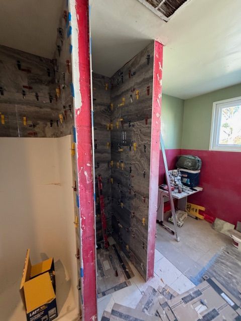 Bathroom under construction with gray tile on the shower walls, red edges, tools and materials scattered.
