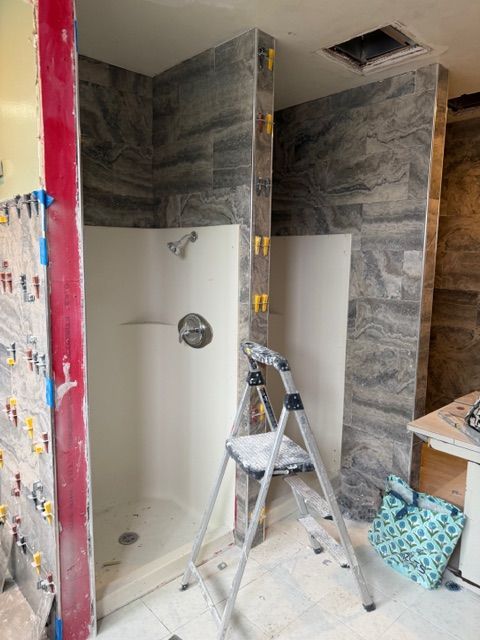 Shower under construction with tiled walls, white base, step ladder, and blue-gray tile.