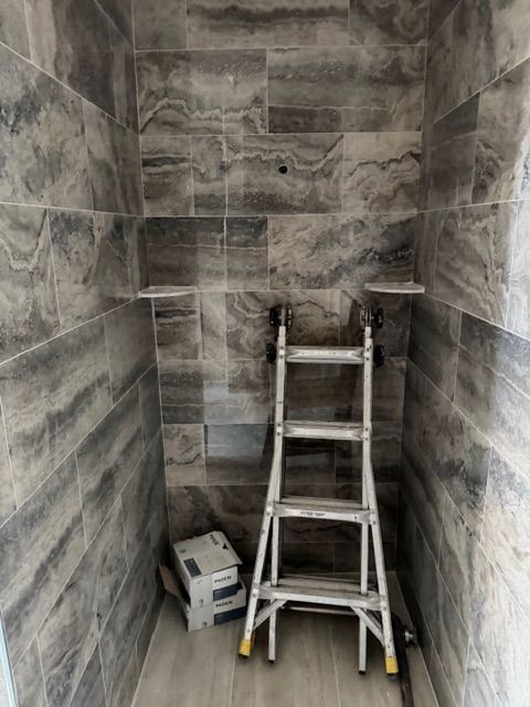 Shower niche with gray tiled walls, two shelves, ladder, and supplies.