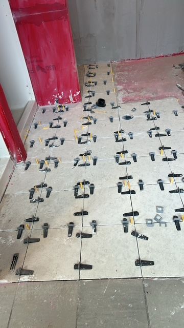 Floor tiles being installed, using leveling clips. Red object leaning against a wall.