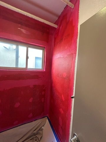A shower alcove with walls coated in pink waterproof membrane and a window above the bathtub.