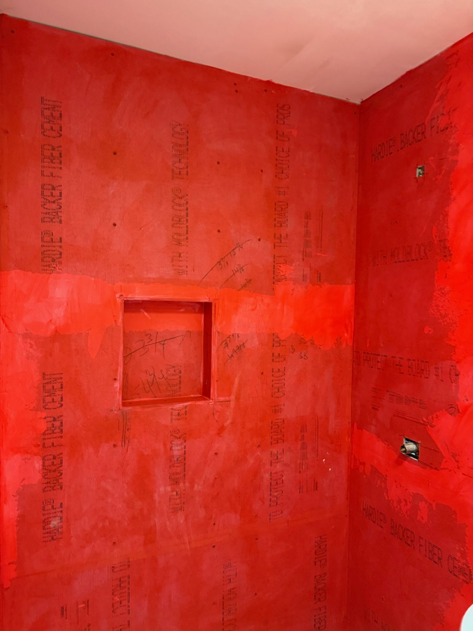 A shower wall alcove covered in bright red waterproofing membrane, showing seams between cement board panels.