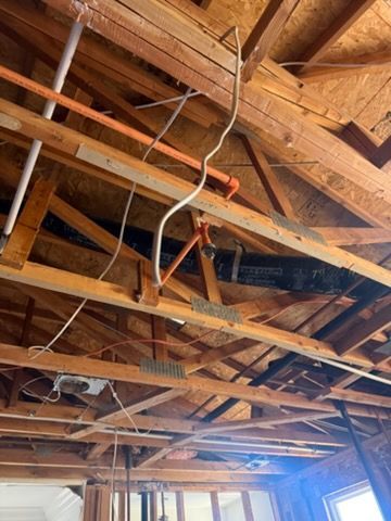 Exposed wooden ceiling rafters, wiring, and black PVC plumbing pipes in an unfinished interior construction space.