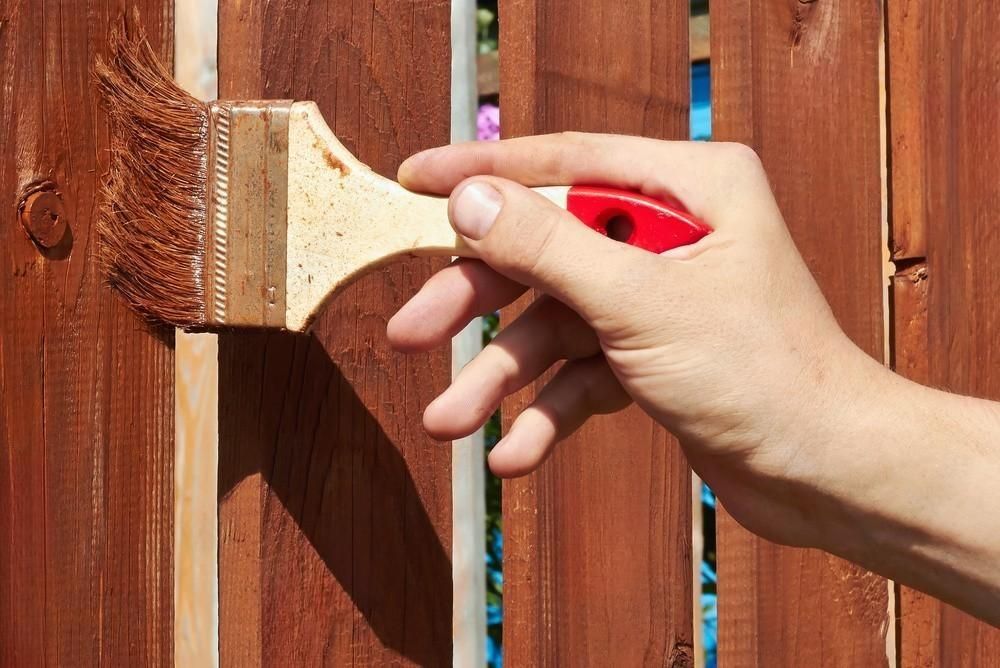 A person is painting a wooden fence with a brush.