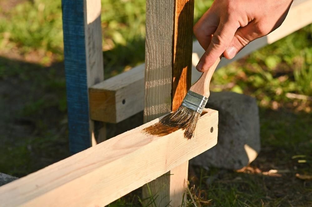 A person is painting a wooden post with a brush.