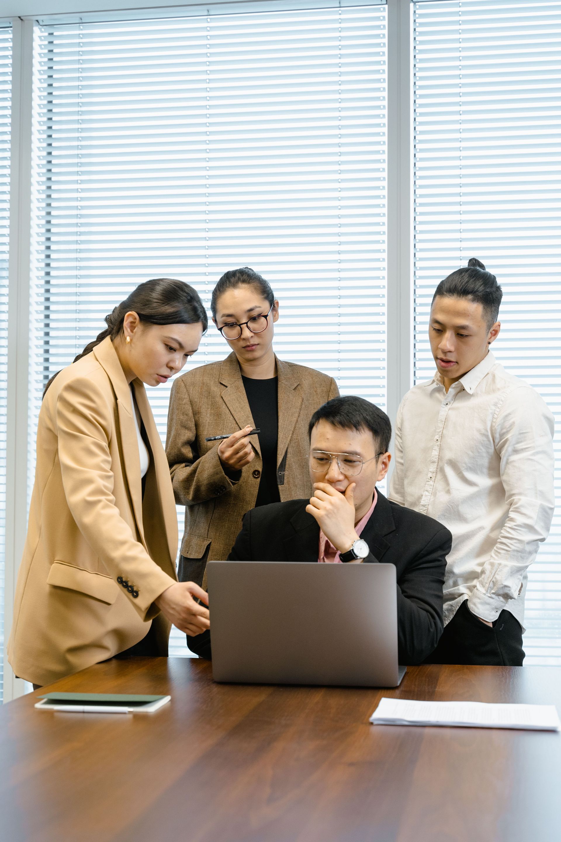 Four coworkers in a meeting around a laptop, discussing in a bright office.