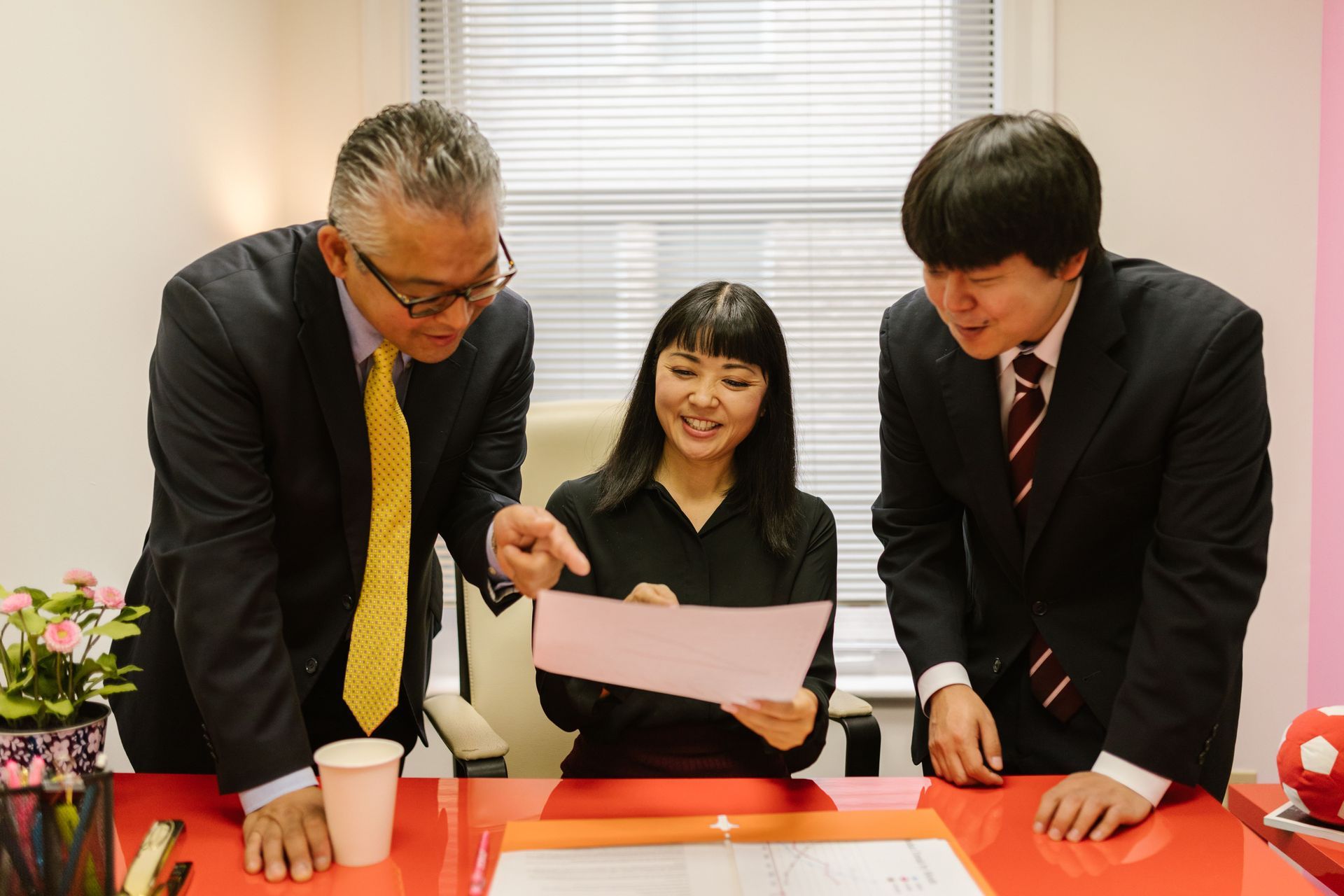 Three coworkers in suits review a document together at a table with papers and flowers.