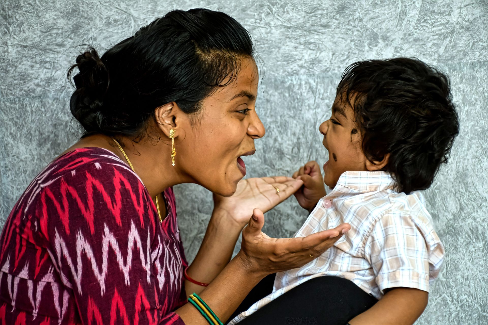 Woman feeding a smiling child by hand against a plain gray background
