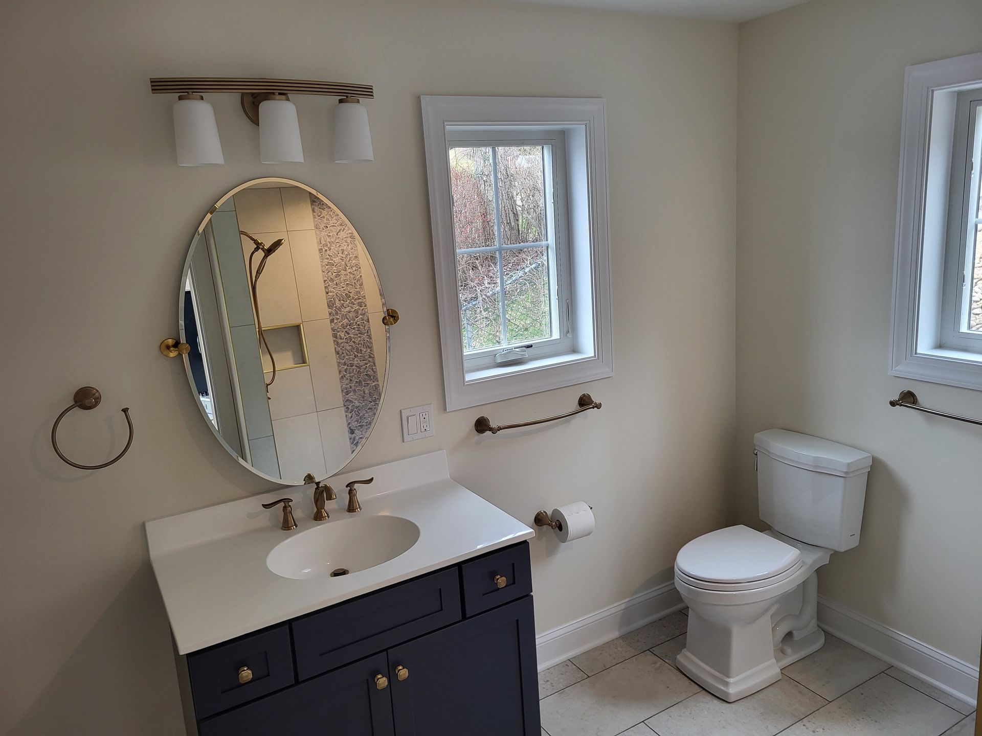 A bathroom with a sink , toilet , mirror and window.