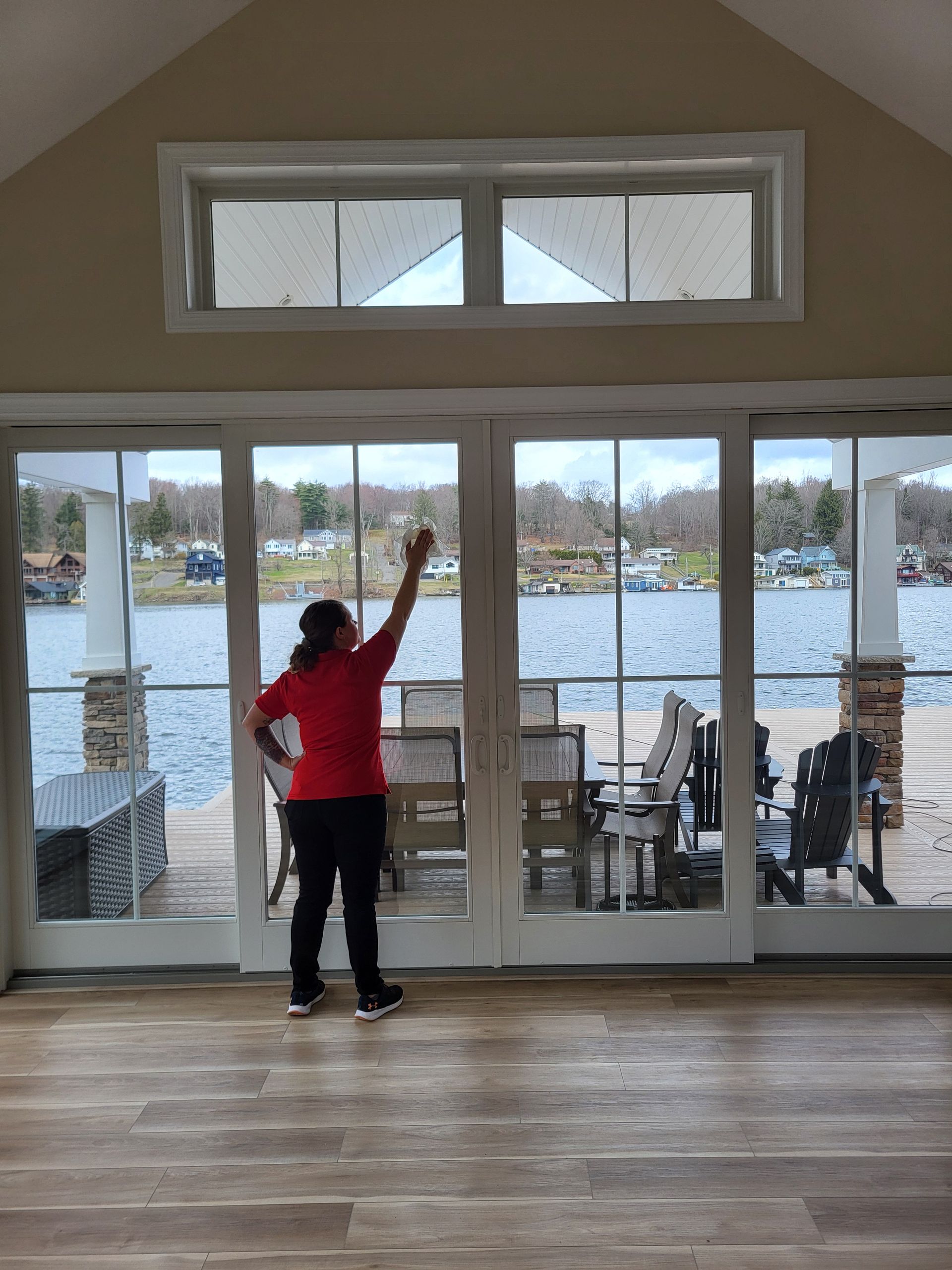 A woman in a red shirt is cleaning a window in a living room.