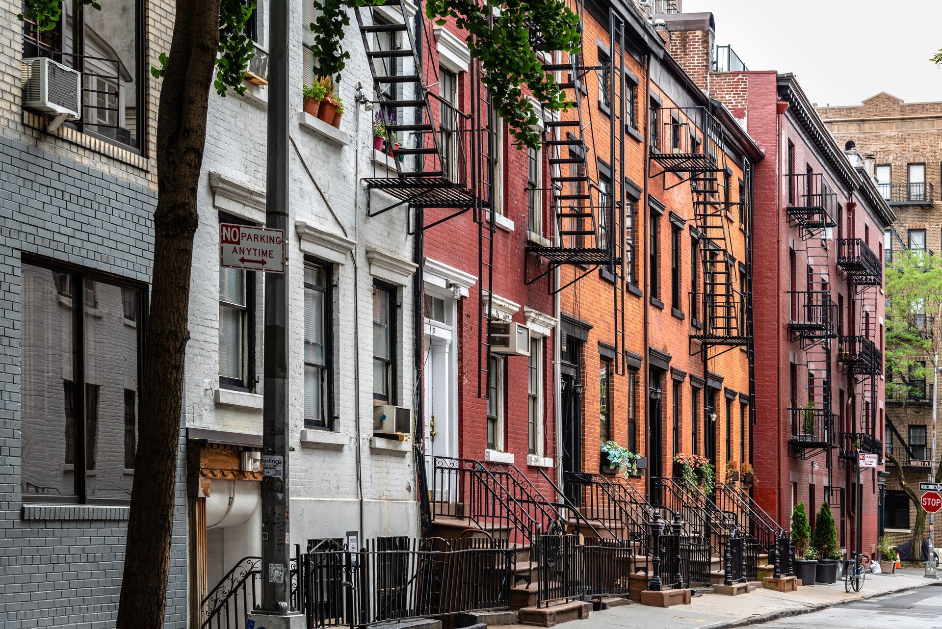 Colorful row of narrow brick townhouses on a quiet city street with fire escapes and parked cars