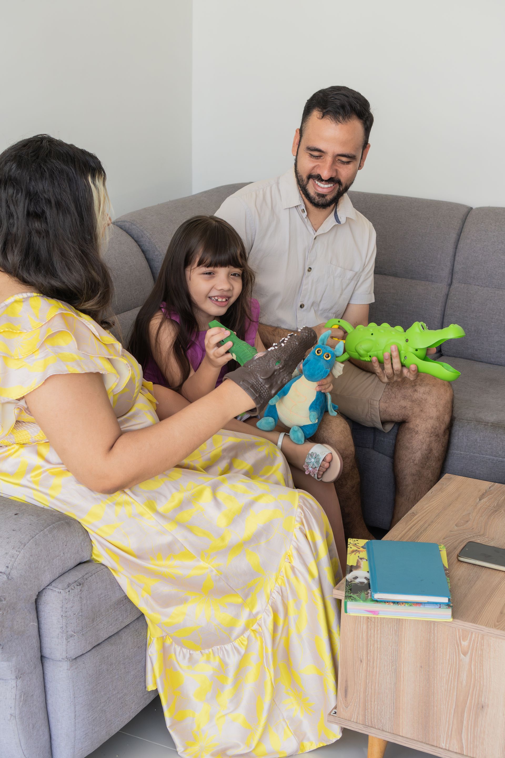 Family sitting on a gray couch, smiling and playing with colorful toys in a bright living room