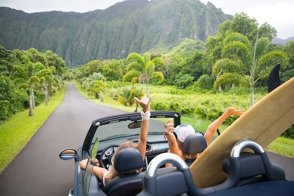 A group of people are riding in a convertible car with a surfboard in the back seat. | Lex Brodies