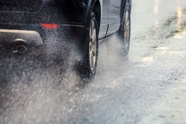 A car is driving through a puddle of water on a wet road. | Lex Brodies